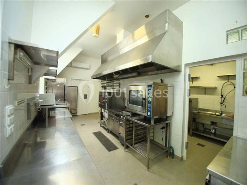 Cuisine professionnelle équipée avec plans de travail en inox, fours, hotte d'extraction et évier en arrière-plan.