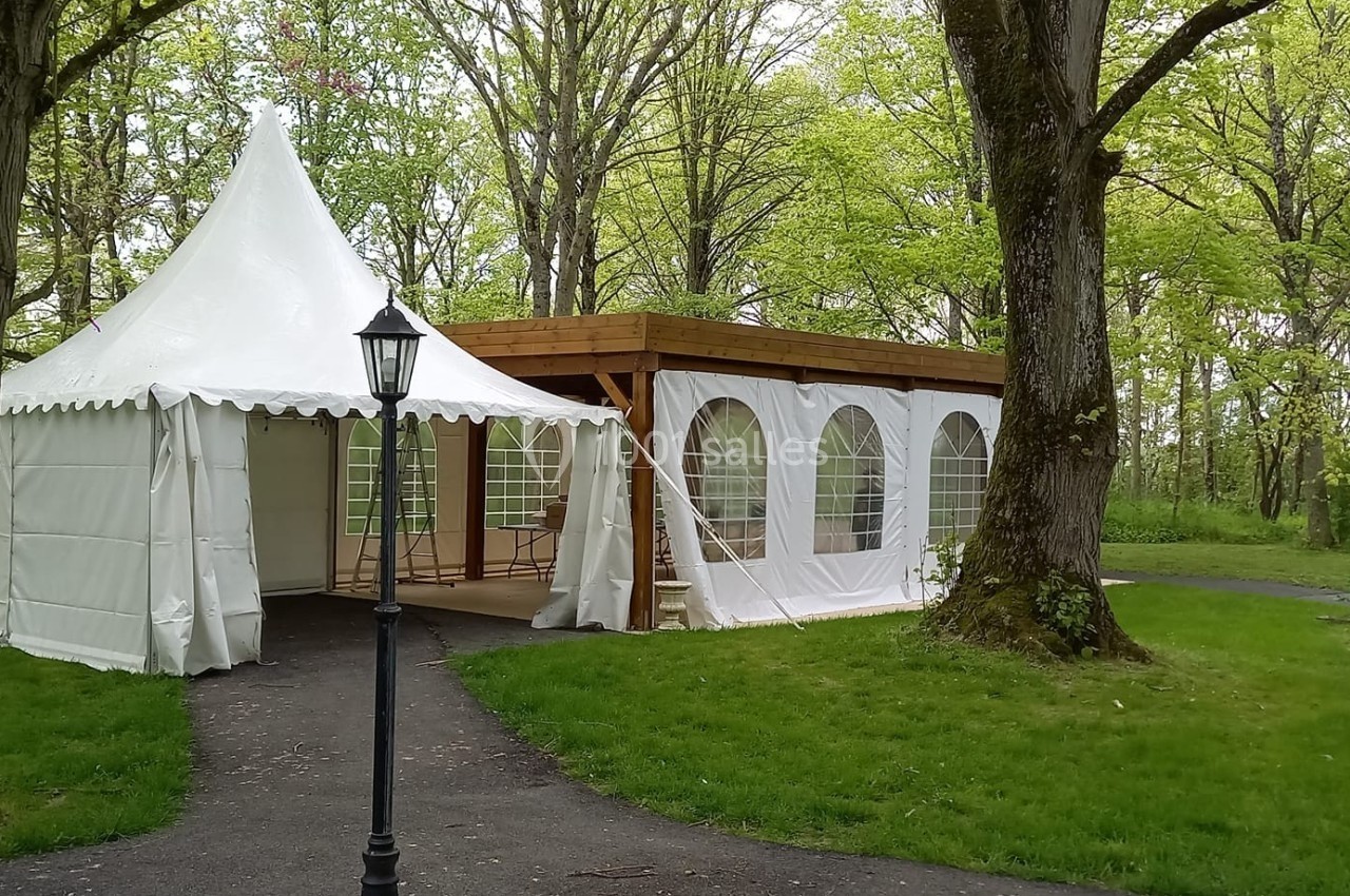 Deux tentes blanches installées dans un espace boisé avec des arbres et une allée pavée.