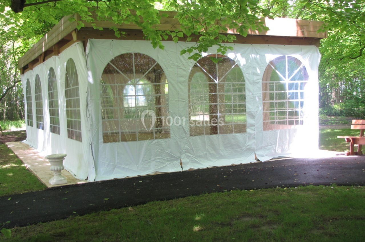 Tente blanche avec fenêtres transparentes installée dans un jardin verdoyant, entourée d'arbres et d'une allée pavée.