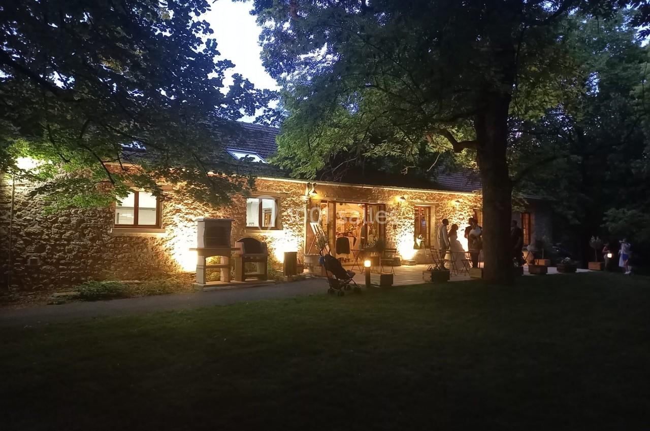 Bâtiment en pierre éclairé à la tombée de la nuit, entouré d'arbres et d'une pelouse sombre.