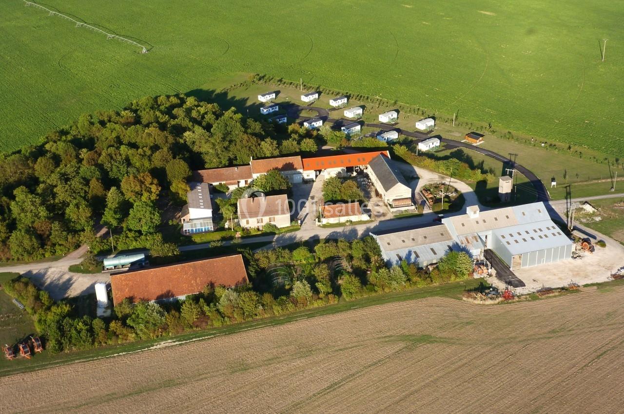 Vue aérienne d'une ferme avec bâtiments, champs cultivés, espaces verts et caravanes stationnées à proximité.