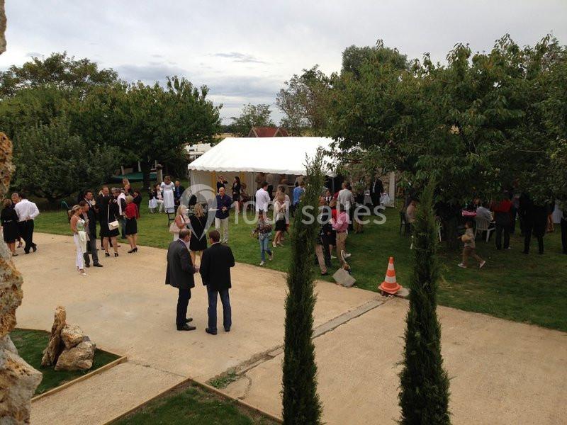 Groupe de personnes rassemblées autour d'une tente blanche dans un jardin lors d'un événement en plein air.
