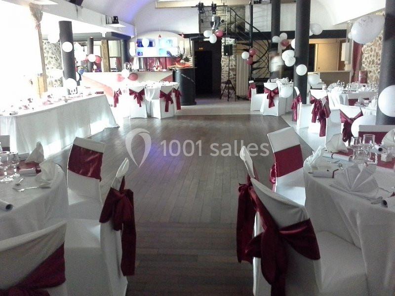 Salle de réception décorée avec des nappes blanches et des nœuds rouges, tables dressées pour un événement festif.