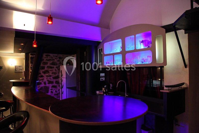 Bar moderne avec comptoir en bois, éclairage coloré violet et rouge, étagères rétroéclairées avec verres.