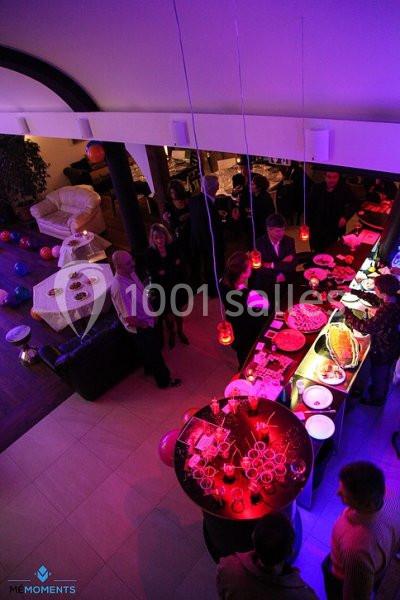 Vue plongeante d'une réception avec buffet illuminé, invités debout discutant dans une ambiance tamisée.