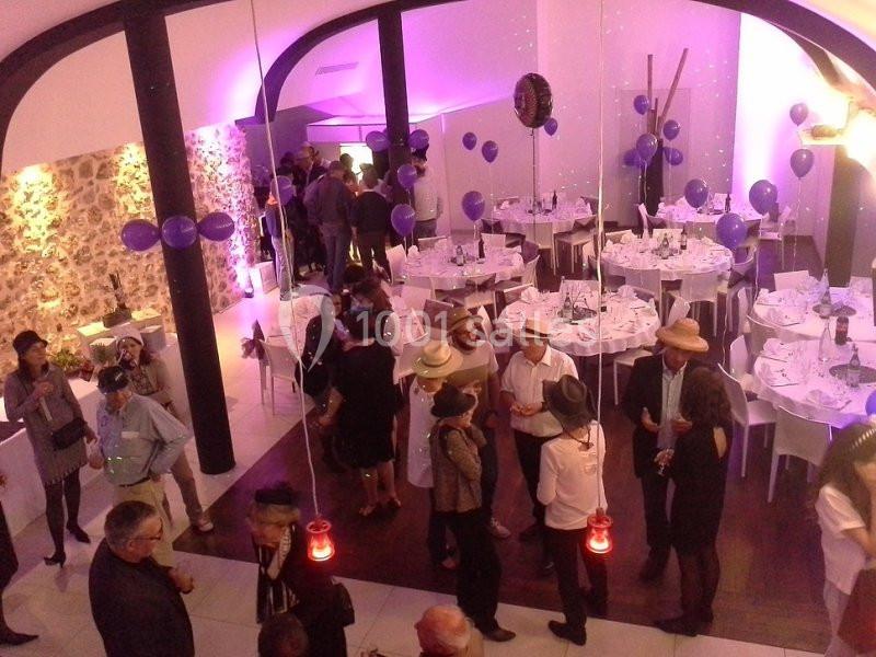 Groupe de personnes discutant dans une salle décorée avec des ballons violets et des tables dressées pour un événement.
