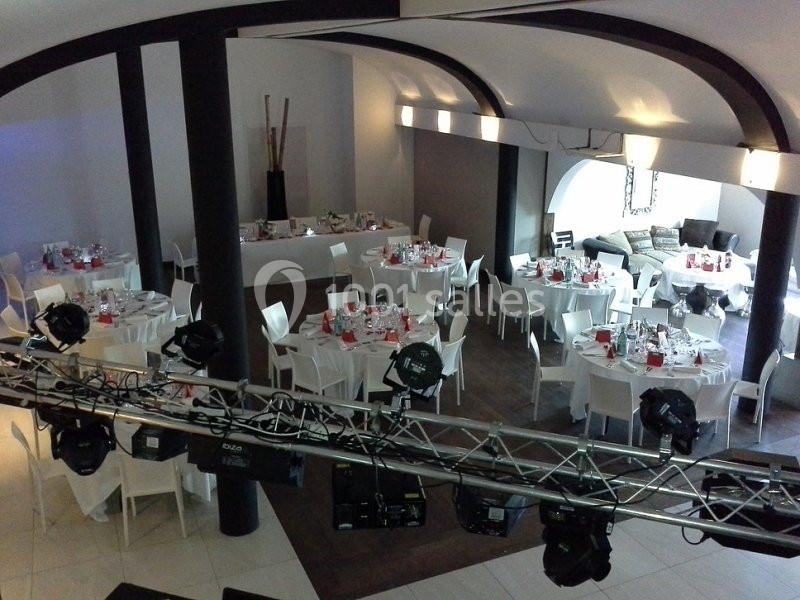 Salle de réception avec tables rondes dressées pour un événement, éclairage suspendu et décoration moderne.