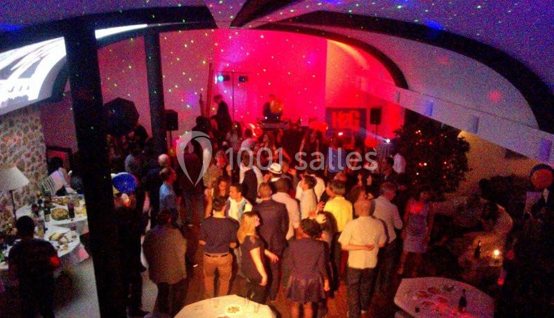 Groupe de personnes dans une salle éclairée par des lumières colorées, avec un DJ en arrière-plan.