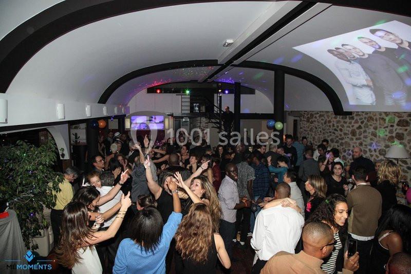 Foule de personnes dans une salle festive, dansant et socialisant sous des lumières colorées.