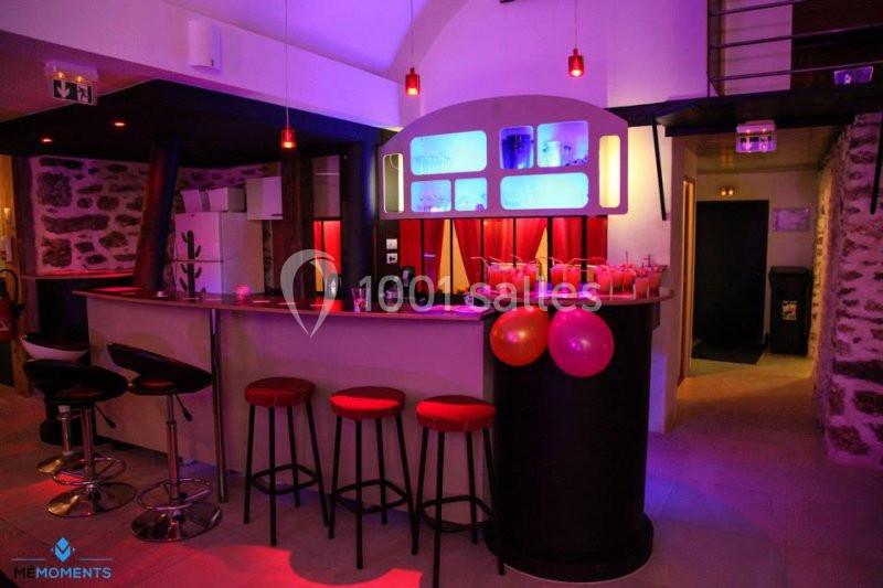 Bar intérieur avec tabourets rouges, comptoir éclairé, décor coloré et ambiance lumineuse tamisée.