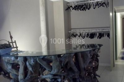 Comptoir en verre avec base en bois sculpté, entouré de portants métalliques avec des cintres noirs dans un espace moderne.