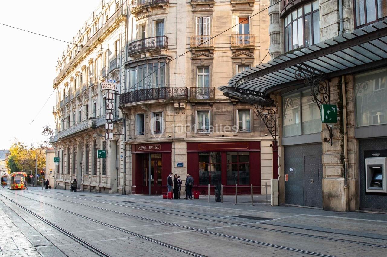 Façade d'un hôtel et bâtiments anciens bordant une rue avec des rails de tramway, quelques passants visibles.