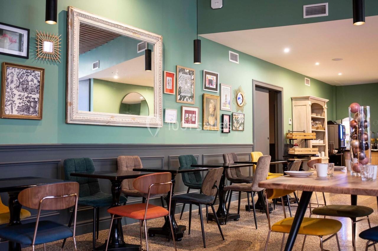 Salle de restaurant moderne avec murs verts, tables en bois, chaises colorées et décorations murales variées.