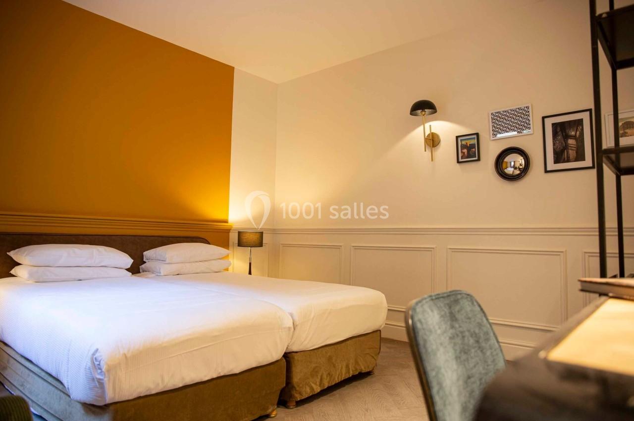 Chambre d'hôtel lumineuse avec deux lits simples, murs blancs et jaunes, décor minimaliste et bureau en bois.