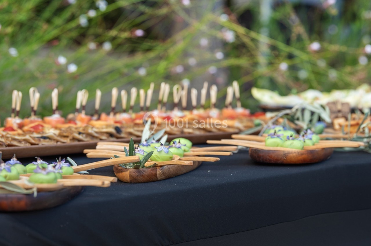 Plateau de bouchées apéritives variées présentées sur une table noire en extérieur, décorée de végétation.