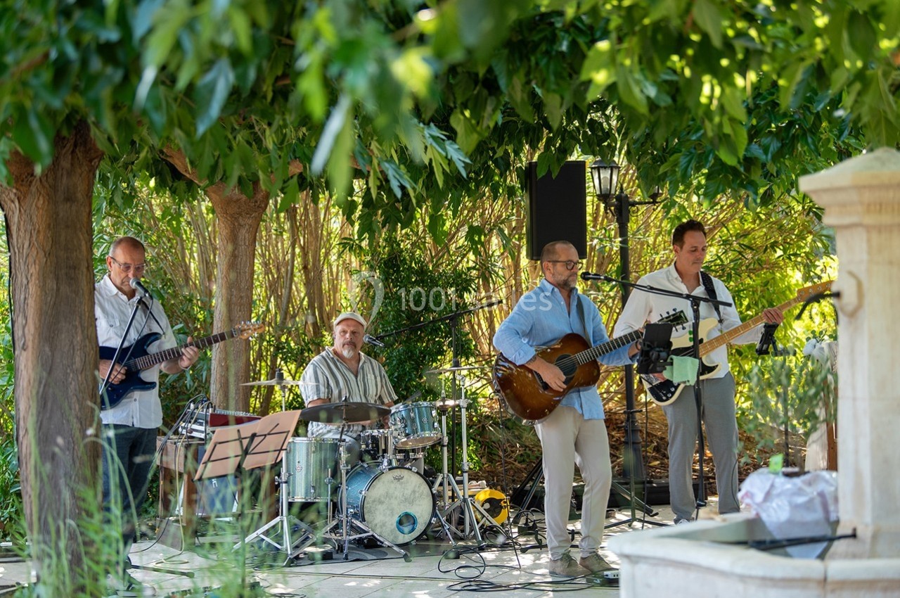 Un groupe de musiciens joue en plein air sous des arbres, entouré de verdure.