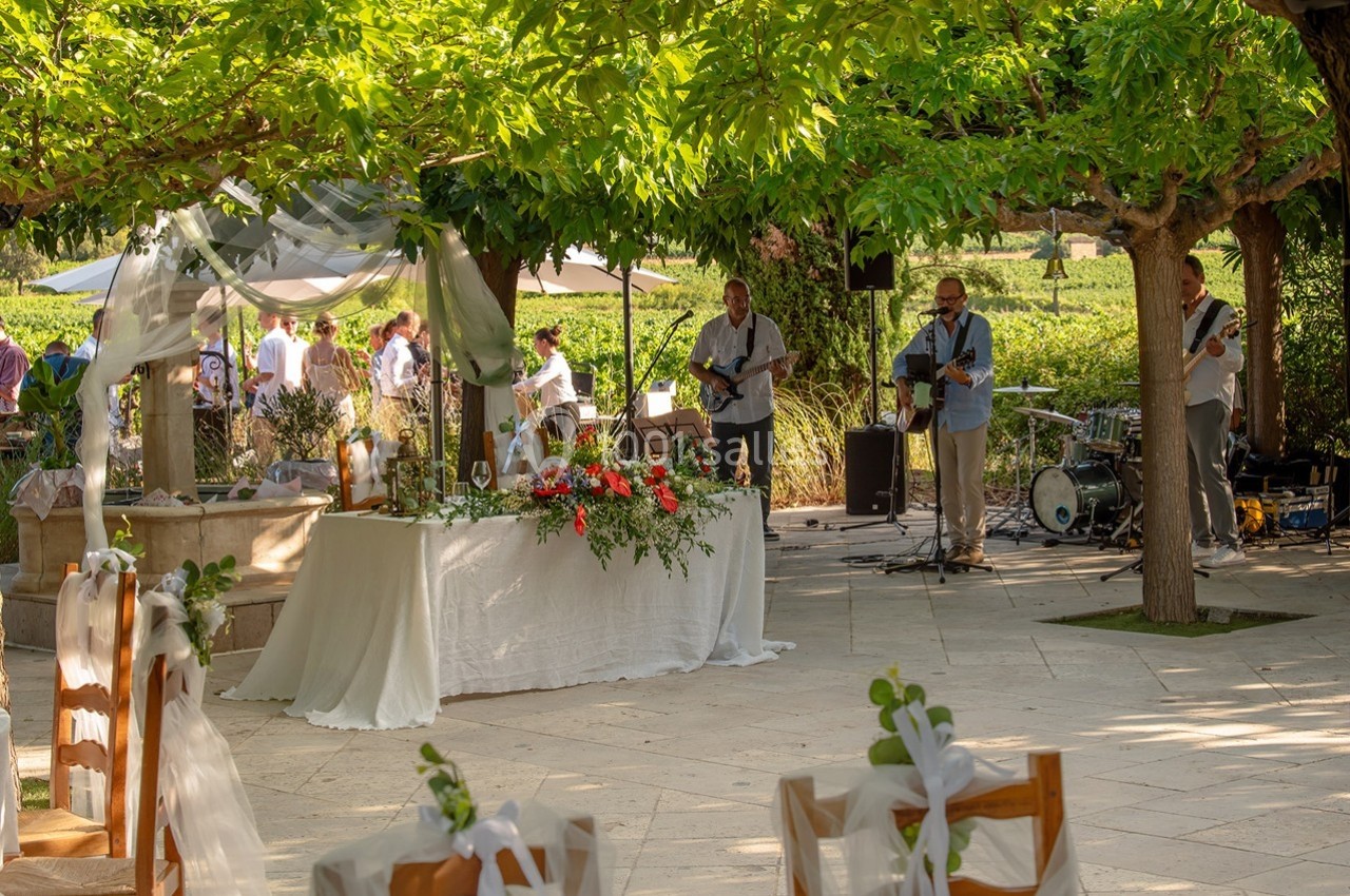 Un groupe de musiciens joue en plein air près d'une table décorée pour un événement, entouré de verdure.