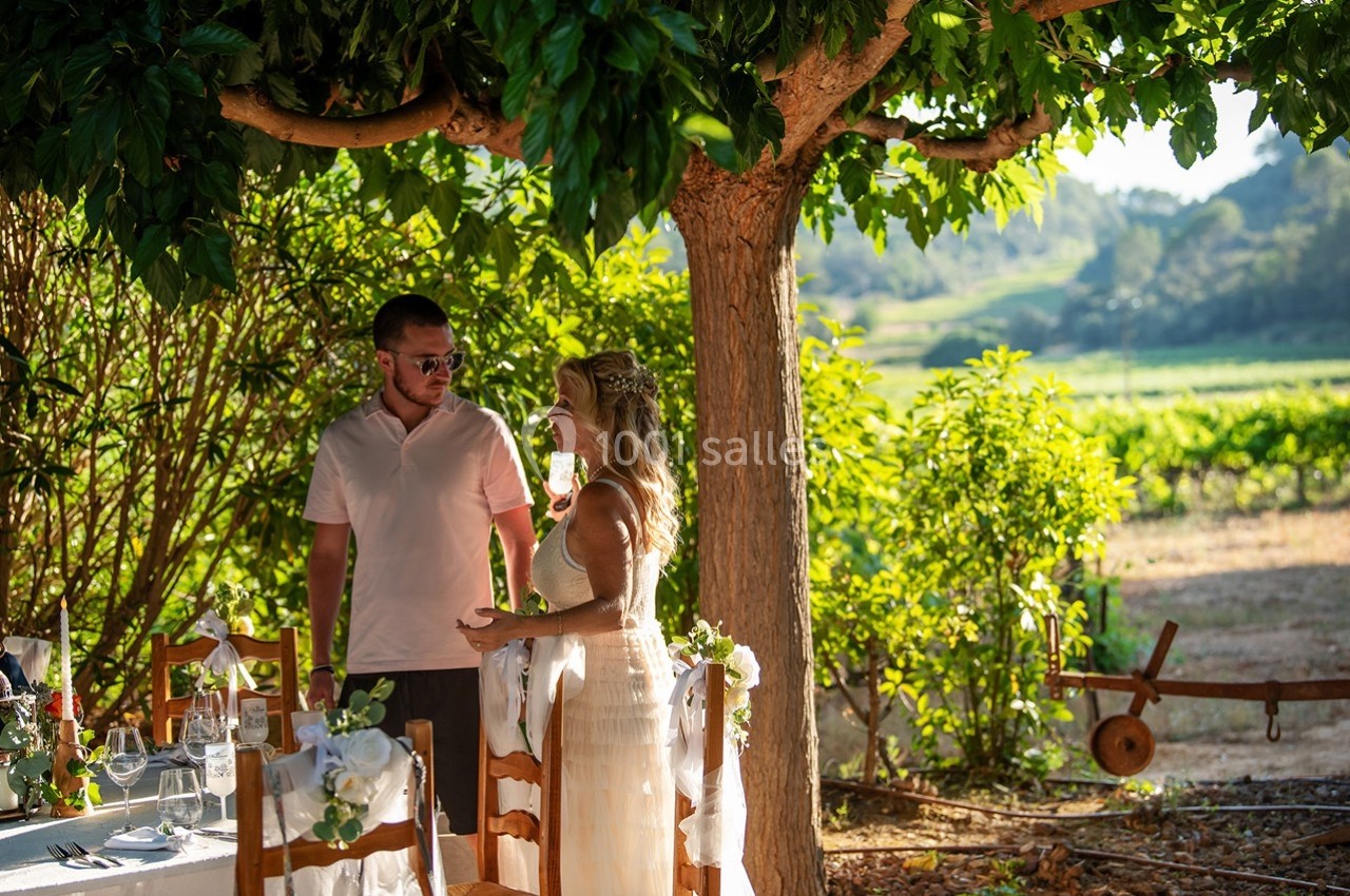 Un couple discute près d'une table décorée sous un arbre, dans un cadre champêtre et ensoleillé.