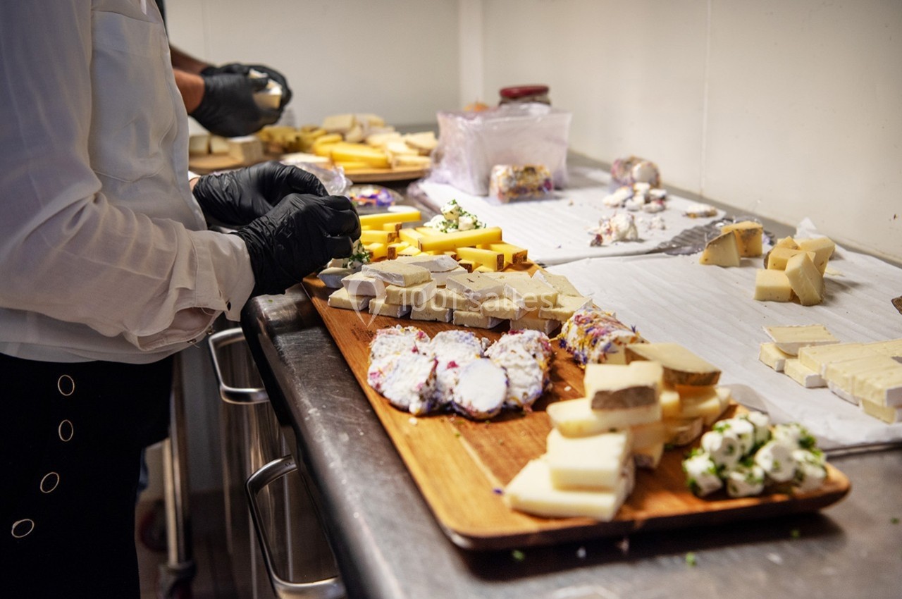 Personnes préparant un plateau de fromages variés sur un plan de travail en cuisine.