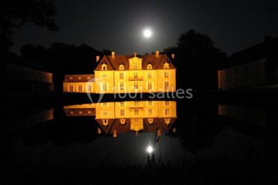 Salle de réception lumineuse avec des tables rondes dressées, nappes blanches et décorations rouges, poutres apparentes.