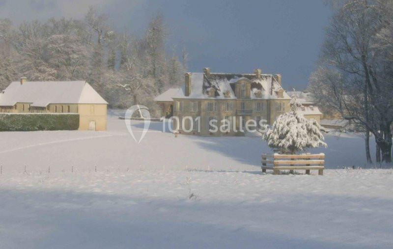 Manoir entouré de bâtiments annexes dans un paysage enneigé sous un ciel partiellement dégagé.
