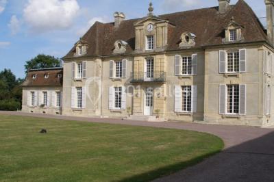 Salle de réception lumineuse avec des tables rondes dressées, nappes blanches et décorations rouges, poutres apparentes.