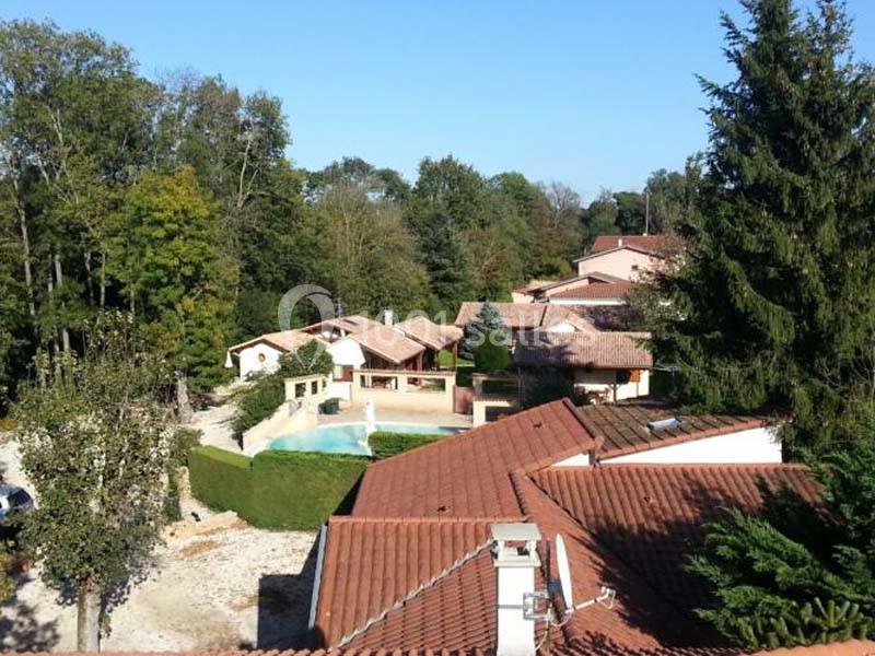 Vue aérienne d'un ensemble de maisons avec toits en tuiles rouges, entourées d'arbres et d'une piscine au centre.