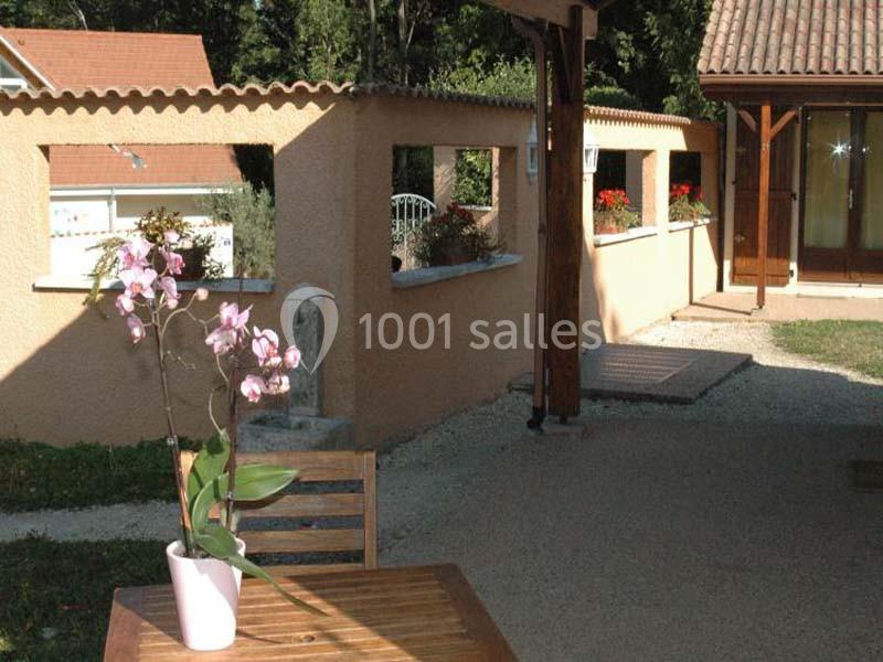 Une orchidée rose en pot posée sur une table en bois dans une cour extérieure ensoleillée avec des murs en crépi beige.