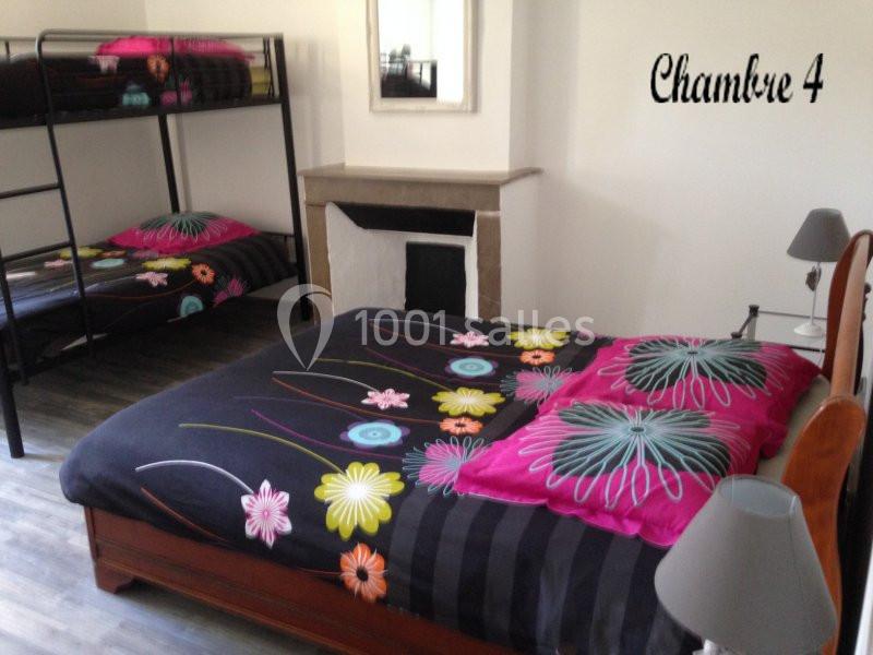 Lit double et lits superposés dans une chambre lumineuse avec cheminée, miroir et décoration florale colorée.