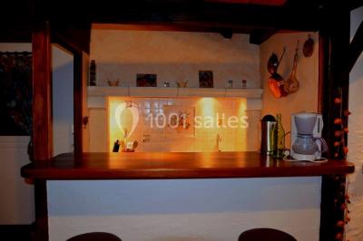 Cuisine rustique avec un bar en bois, éclairage chaleureux, cafetière et ustensiles suspendus au mur.