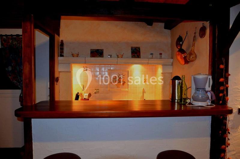 Cuisine rustique avec un bar en bois, éclairage chaleureux, cafetière et ustensiles suspendus au mur.