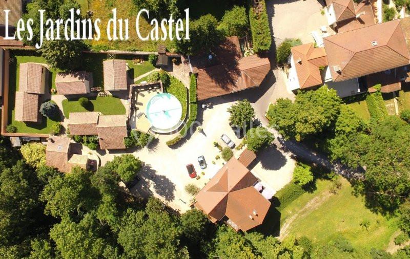 Vue aérienne d'un complexe résidentiel entouré de verdure, avec une piscine centrale et des bâtiments en toits rouges.