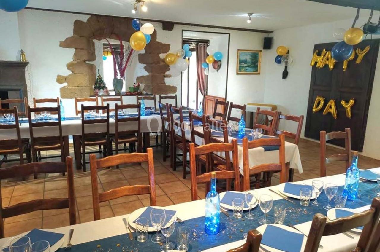 Salle décorée pour une fête avec tables dressées, ballons colorés et guirlande ’Happy Day’ accrochée au mur.