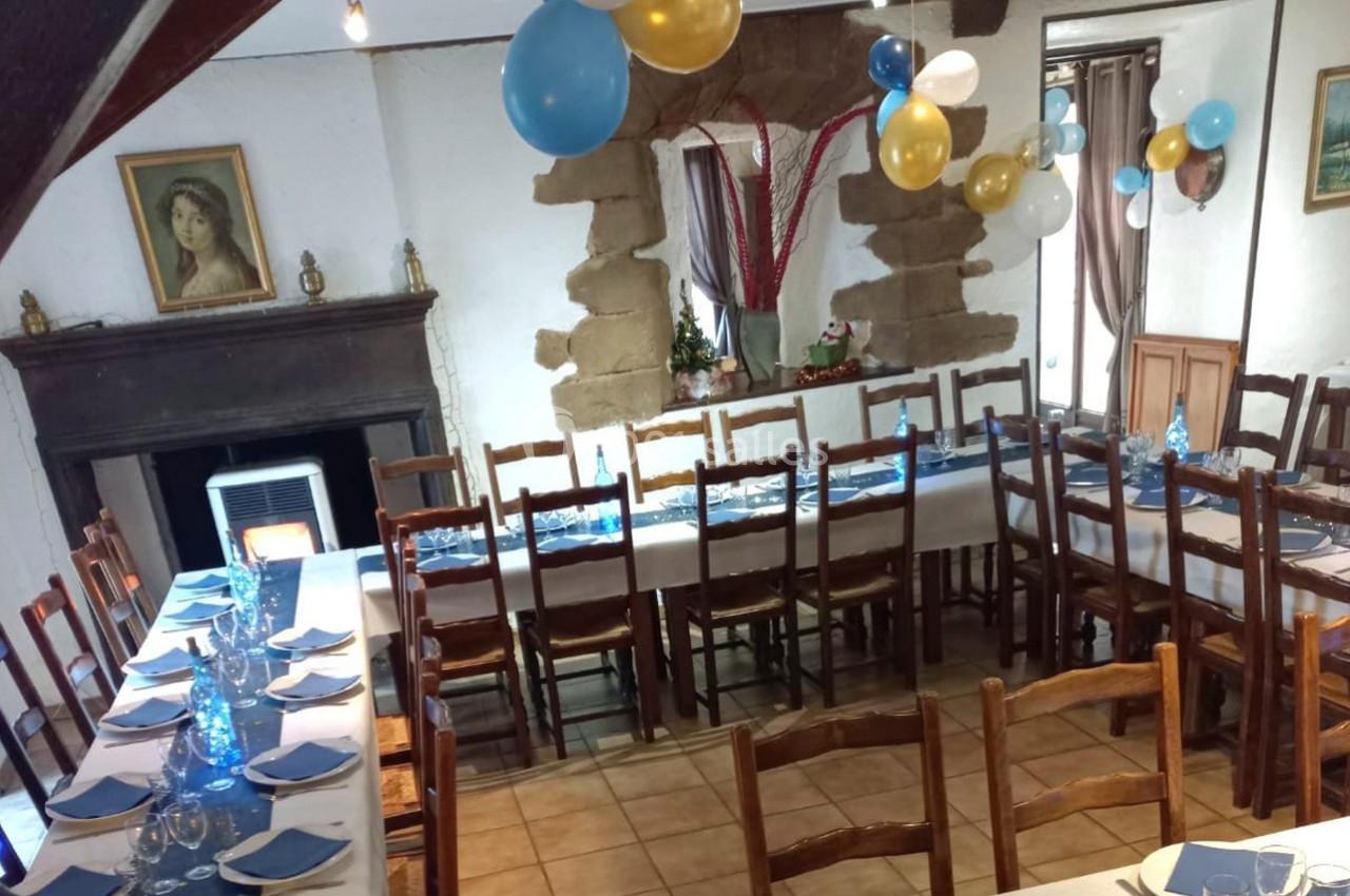 Salle décorée pour un événement avec des tables dressées, des ballons colorés et une cheminée en arrière-plan.