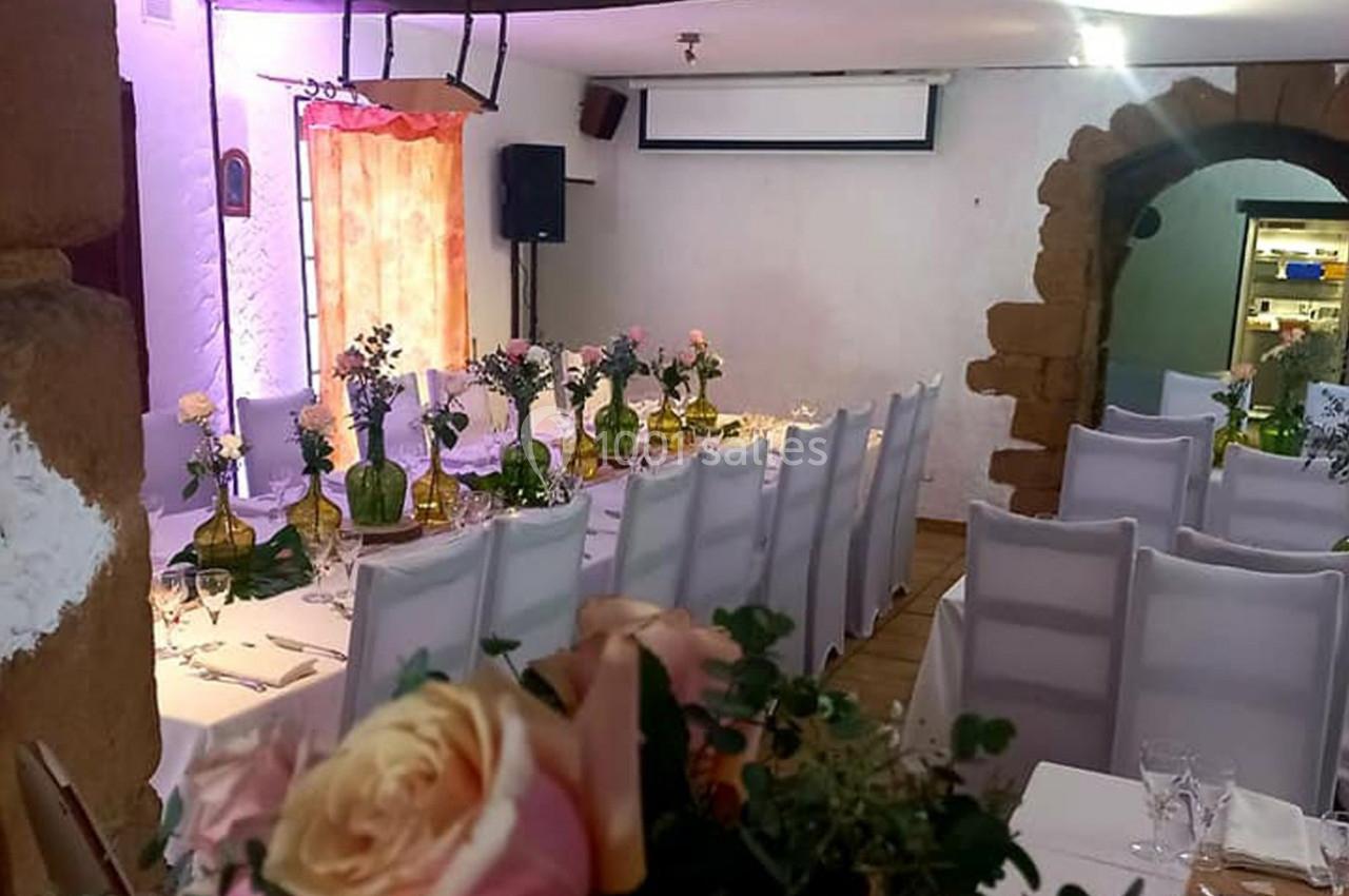Salle décorée pour un événement avec des tables alignées, nappes blanches, chaises houssées et bouquets de fleurs.