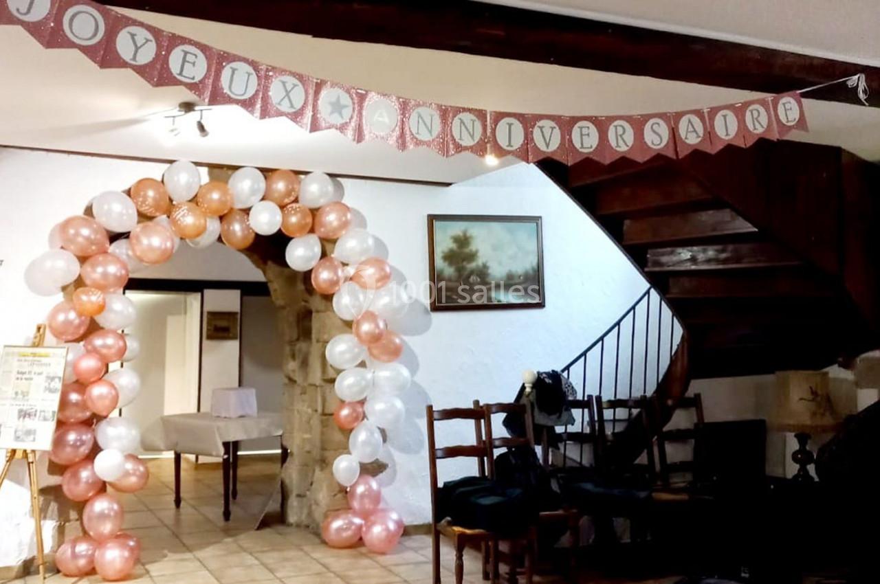 Décoration d'anniversaire avec arche de ballons blancs et roses, guirlande ’Joyeux Anniversaire’ et intérieur rustique.
