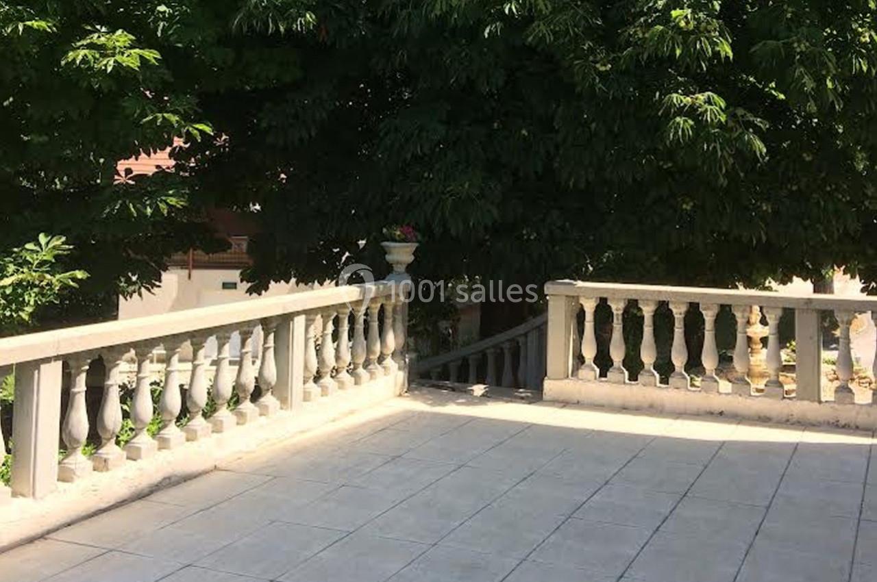 Terrasse en pierre bordée de balustrades blanches, entourée de végétation dense et ombragée.