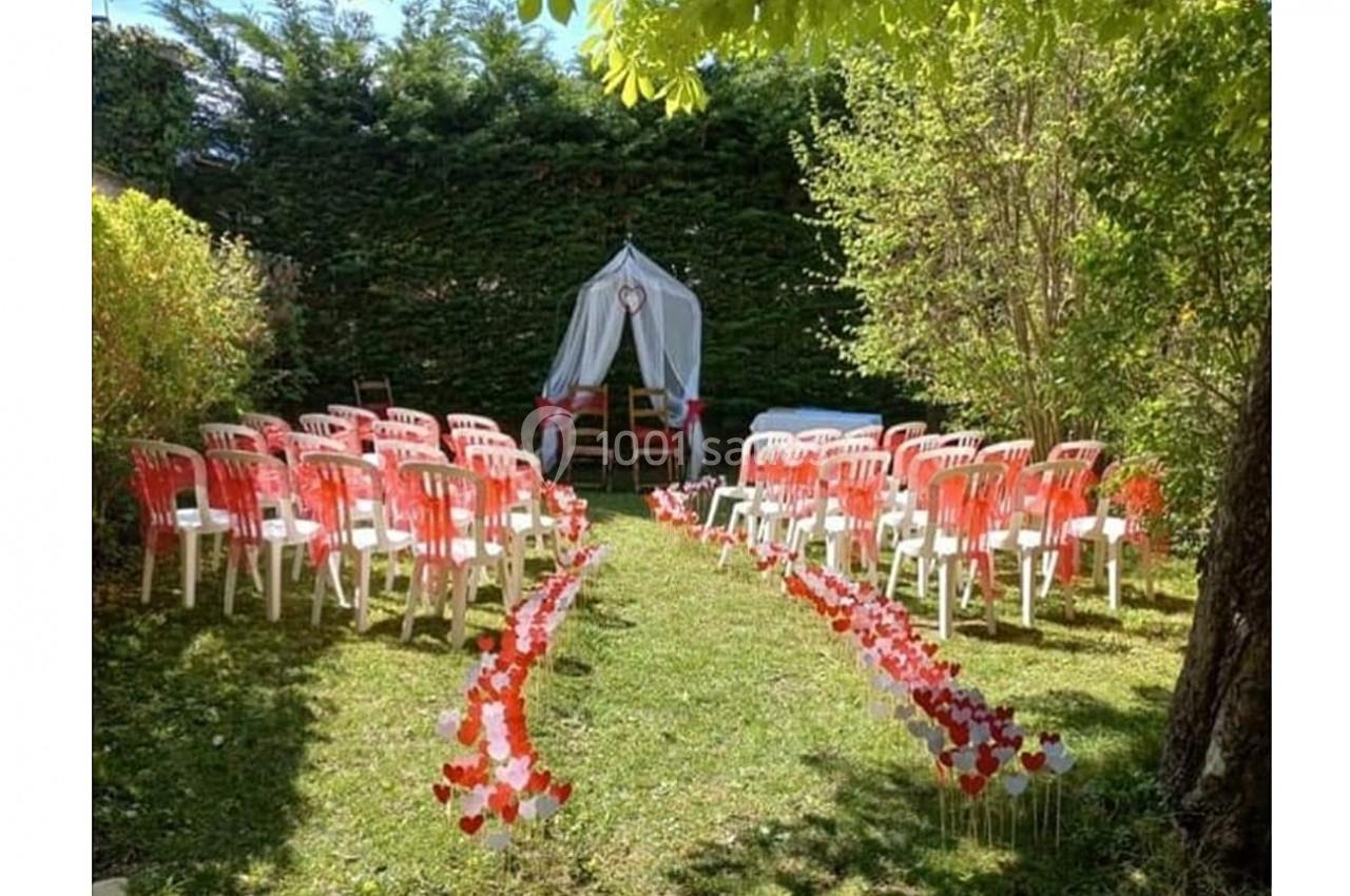 Allée décorée de cœurs menant à une arche blanche entourée de chaises rouges et blanches dans un jardin verdoyant.