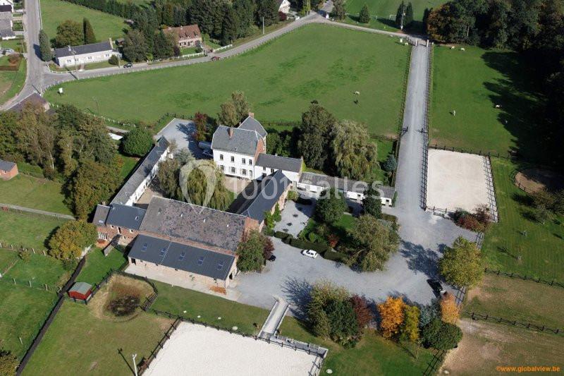 Vue aérienne d'un domaine rural avec bâtiments, cour centrale, carrières équestres et espaces verts environnants.