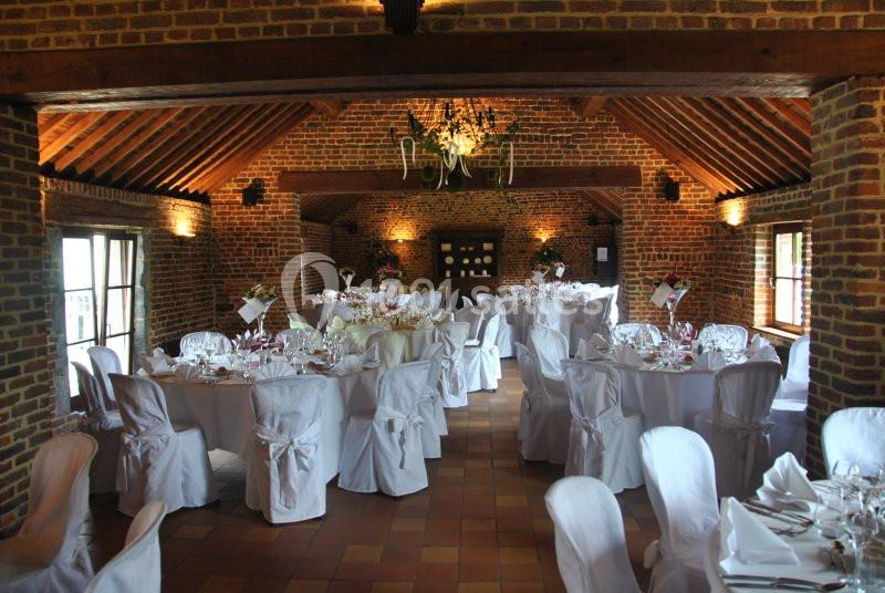 Salle de réception en briques avec tables rondes dressées, nappes blanches et lustre central.