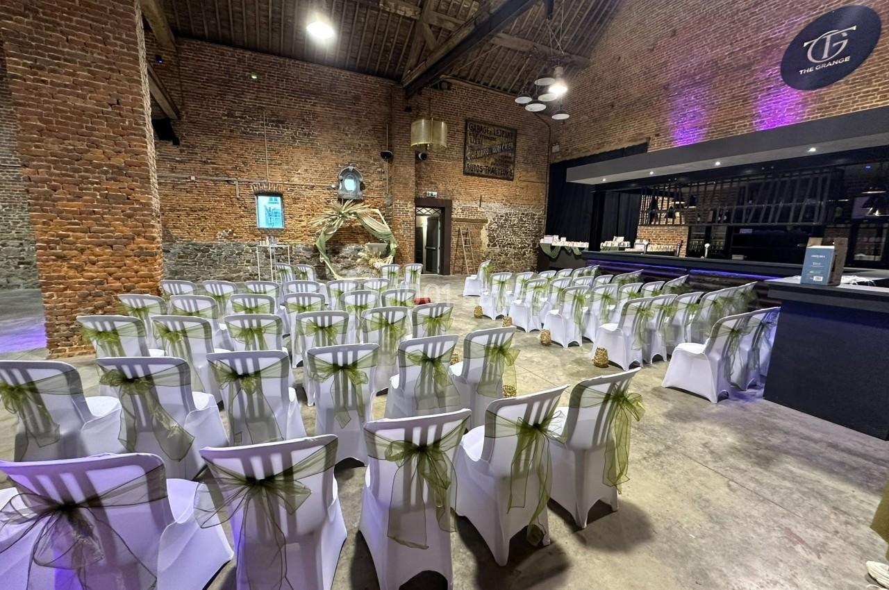 Salle de réception avec des chaises blanches décorées de rubans verts, disposées face à un bar moderne dans un cadre en…