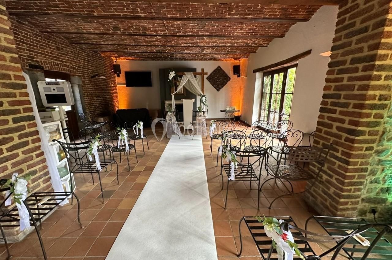 Salle décorée pour une cérémonie, avec chaises en fer forgé, allée centrale blanche et autel orné de fleurs.