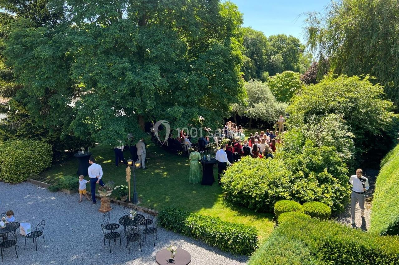Un rassemblement de personnes dans un jardin verdoyant, sous un grand arbre, par une journée ensoleillée.