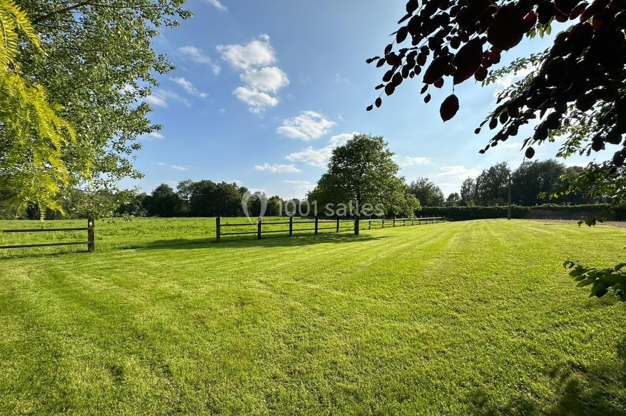 Pelouse verte bien entretenue bordée d'arbres et clôturée, sous un ciel bleu parsemé de nuages.