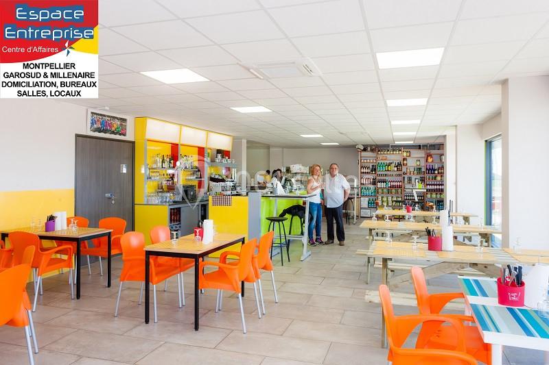 Salle lumineuse avec tables, chaises colorées, espace de restauration et étagères remplies de produits en arrière-plan.
