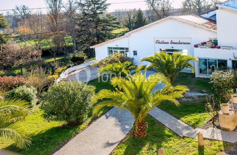 Allée bordée de palmiers menant à un bâtiment blanc entouré de végétation, sous un ciel dégagé.