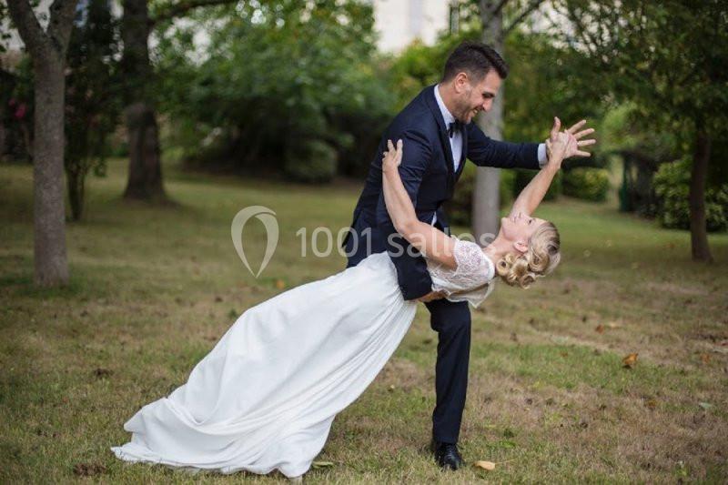 Un couple en tenue de mariage exécute une pose de danse élégante dans un jardin verdoyant.