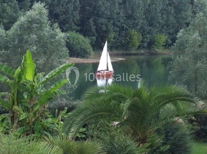 Voilier blanc naviguant sur un lac entouré de végétation luxuriante et d'arbres en arrière-plan.