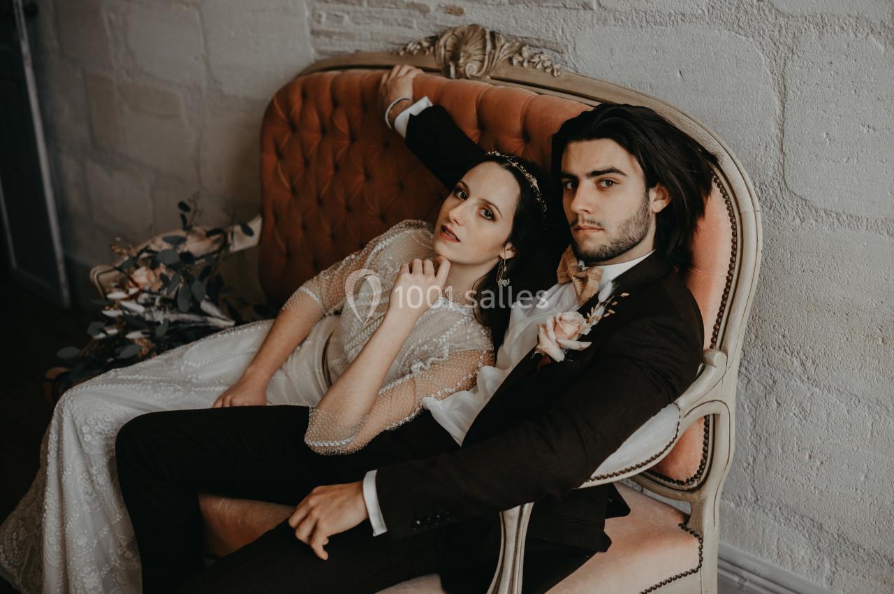 Un couple en tenue de mariage est assis sur un canapé ancien dans un décor intérieur élégant.