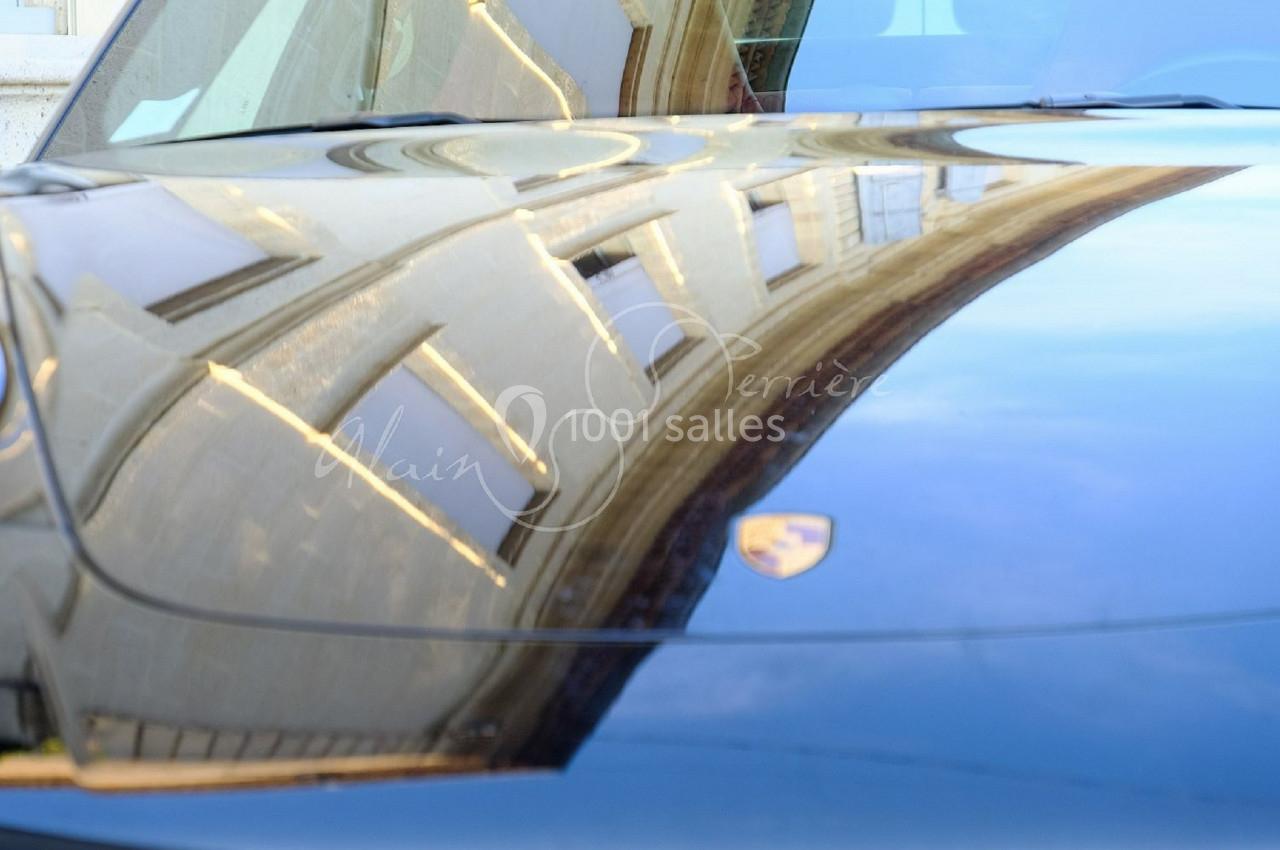 Reflet d'un bâtiment sur le capot brillant d'une voiture noire stationnée.